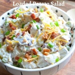 loaded baked potato salad garnished with bacon, cheddar, scallions in a white bowl