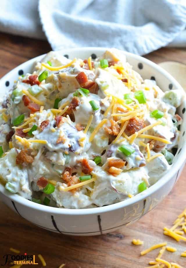 loaded baked potato salad in a white bowl garnished with bacon, cheddar & green onion