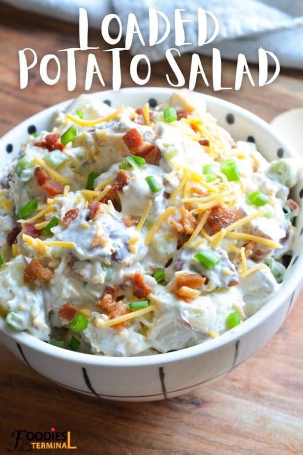 fully loaded red potato salad in a white bowl garnished with crispy bacon, green onion & shredded cheddar cheese.
