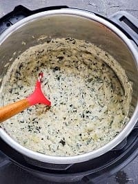 hot spinach artichoke dip in instant pot with a red and wooden ladle