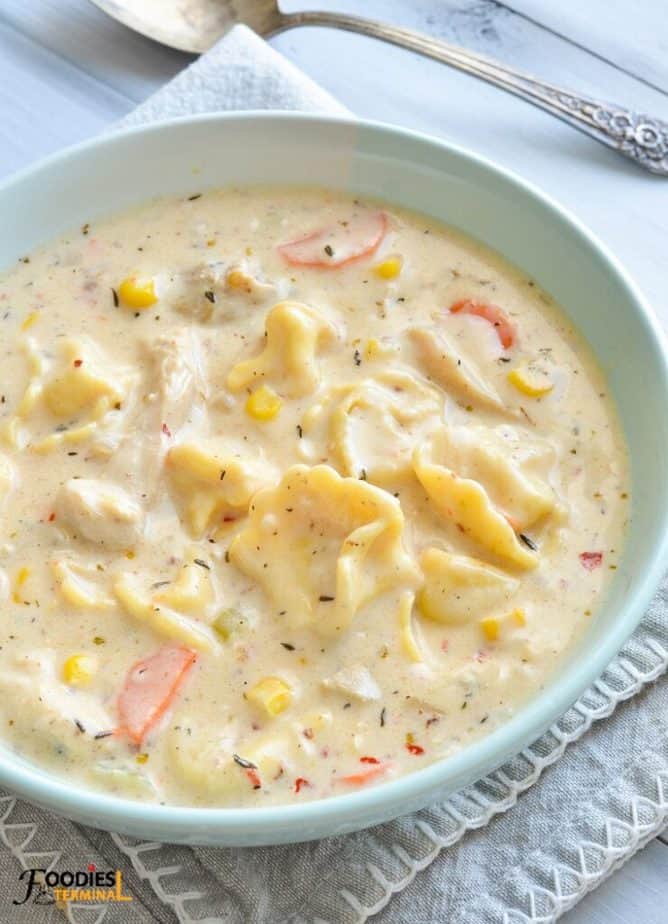 creamy chicken tortellini soup in a light blue bowl placed on a grey linen with a silver spoon at the background