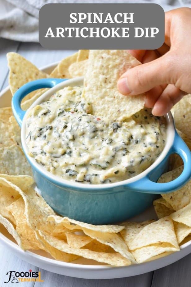 easy spinach artichoke dip served in a small turquoise bowl & a tortilla chip being dipped into the dip along with other tortillas surrounding the main dip