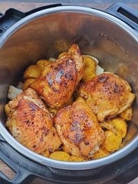 seared chicken thighs layered on top of the potatoes in the pot