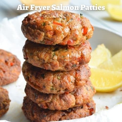 air fryer salmon patties stacked on a white plate with lemon wedges on the background