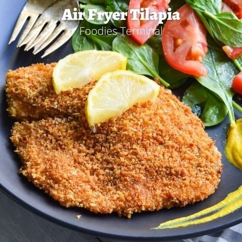 air fryer panko crusted tilapia garnished with lemon slices & served with a salad on the side on a black plate with forks & mustard sauce