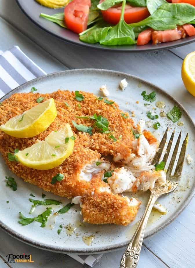 air fryer tilapia panko crusted garnished with parsley & lemon slices on a grey plate with a fork