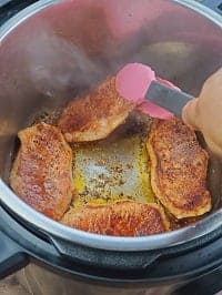searing boneless pork chops in the instant pot with a pink tong