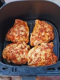seasoned frozen chicken thighs in a single layer inside the air fryer basket