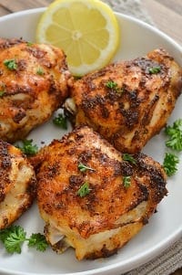 air fryer frozen chicken thighs served with lemon slice and garnished with chopped parsley on a white plate