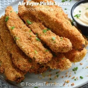 air fryer fried pickles with dipping sauce on a grey plate garnished with fresh chopped parsley