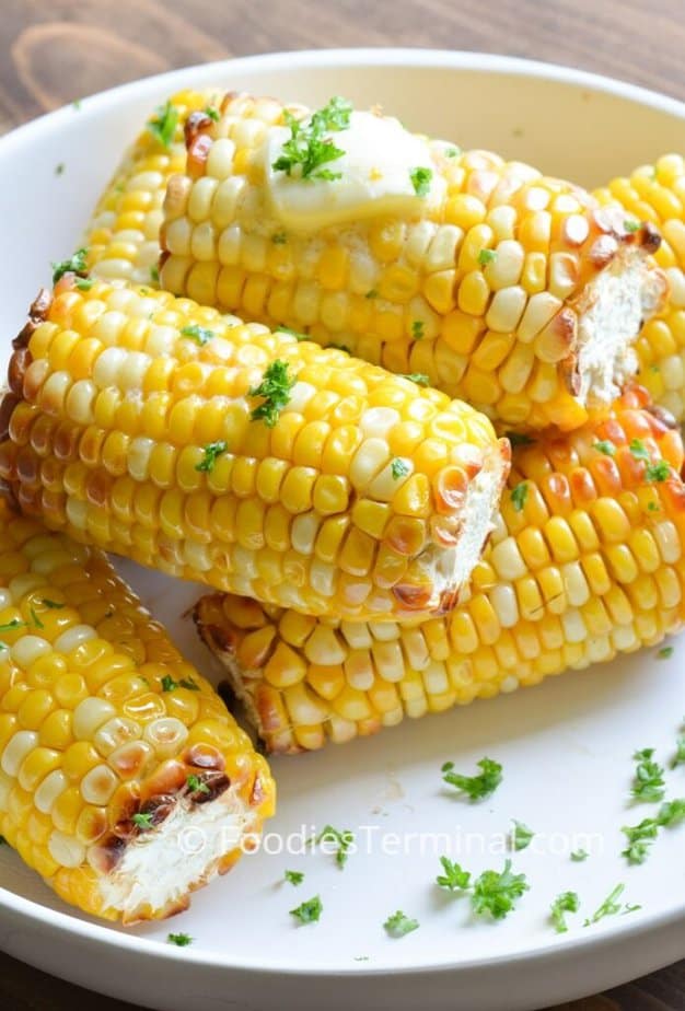 air fryer corn on the cob in a white plate  garnished with butter and fresh chopped parsley