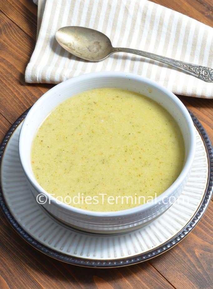 zucchini soup creamy in a white bowl with a spoon in the back drop