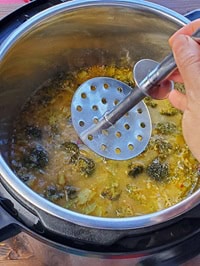 mashing cooked broccoli with steel potato masher