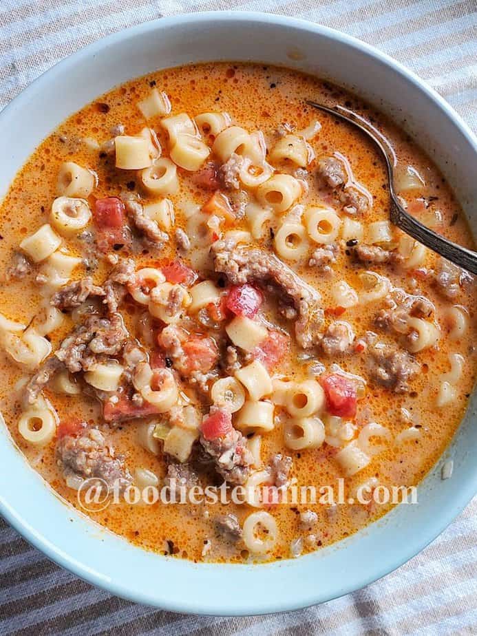 Creamy Parmesan Italian Sausage soup in a pale blue bowl with a spoon
